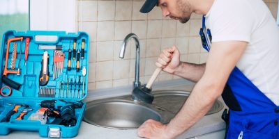 Handyman in uniform is cleaning a clogged kitchen sink with the help of plunger