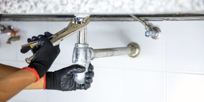 Plumber using a wrench to repair a water pipe under the sink.